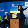纽约州长凯西·霍克尔（Kathy Hochul）在戴斯（Dais）后面说话时用手示意。在背景中，一个大横幅指出，“纽约的第一个离岸农场”南叉风电场的2022年开创性。“loading=