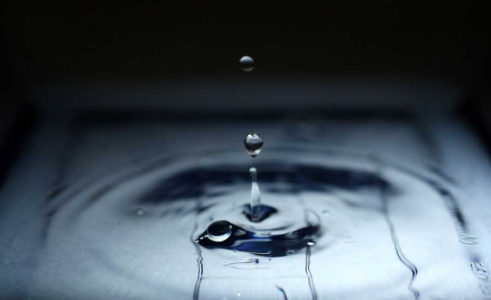 A drop of water splashes up from a larger pool of water